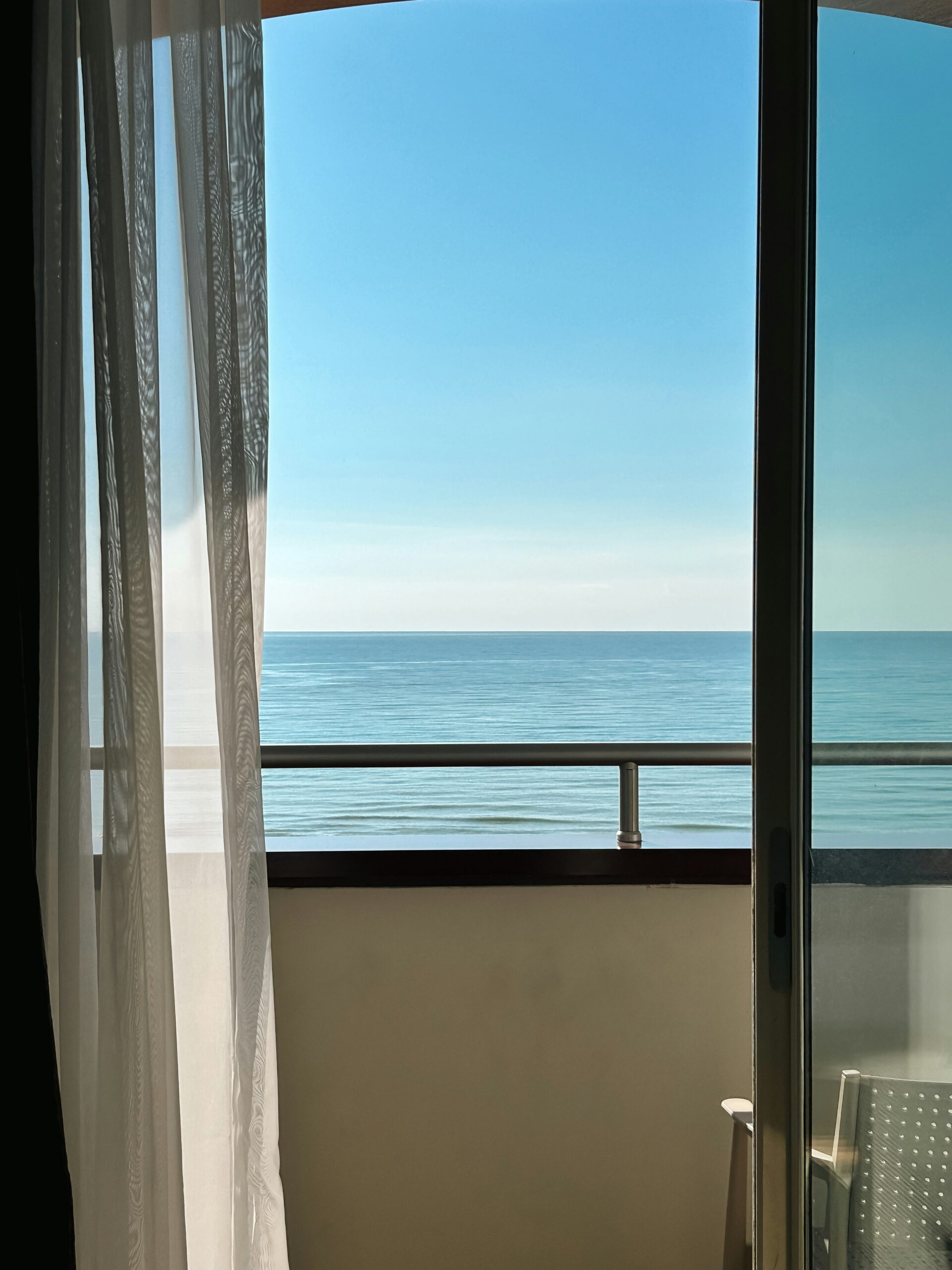 Ocean view through an open balcony door with sheer curtains