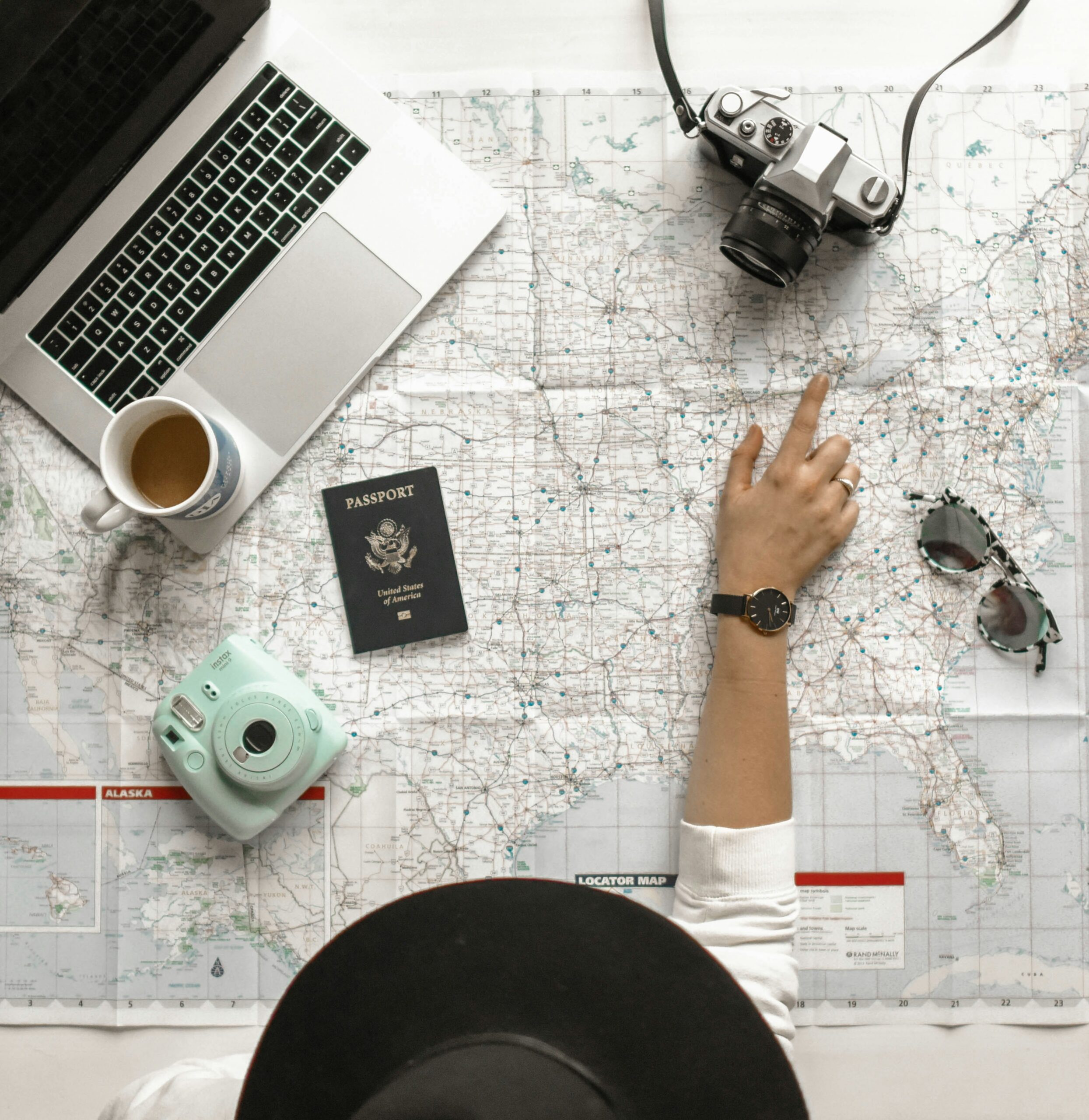 A laptop, coffee, passport, and camera laid out on a map