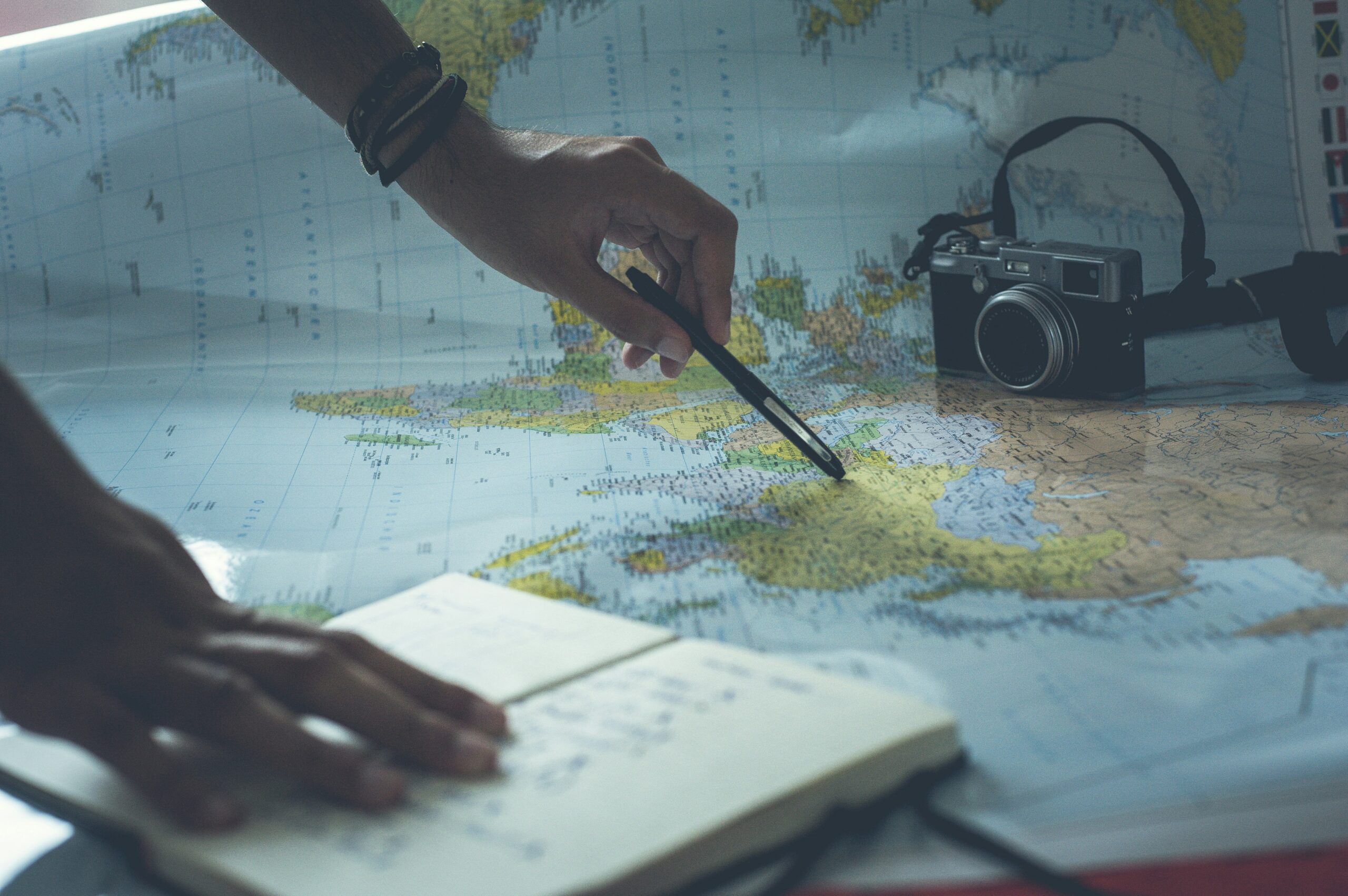 A hand pointing to a spot on a map beside an open notebook and camera