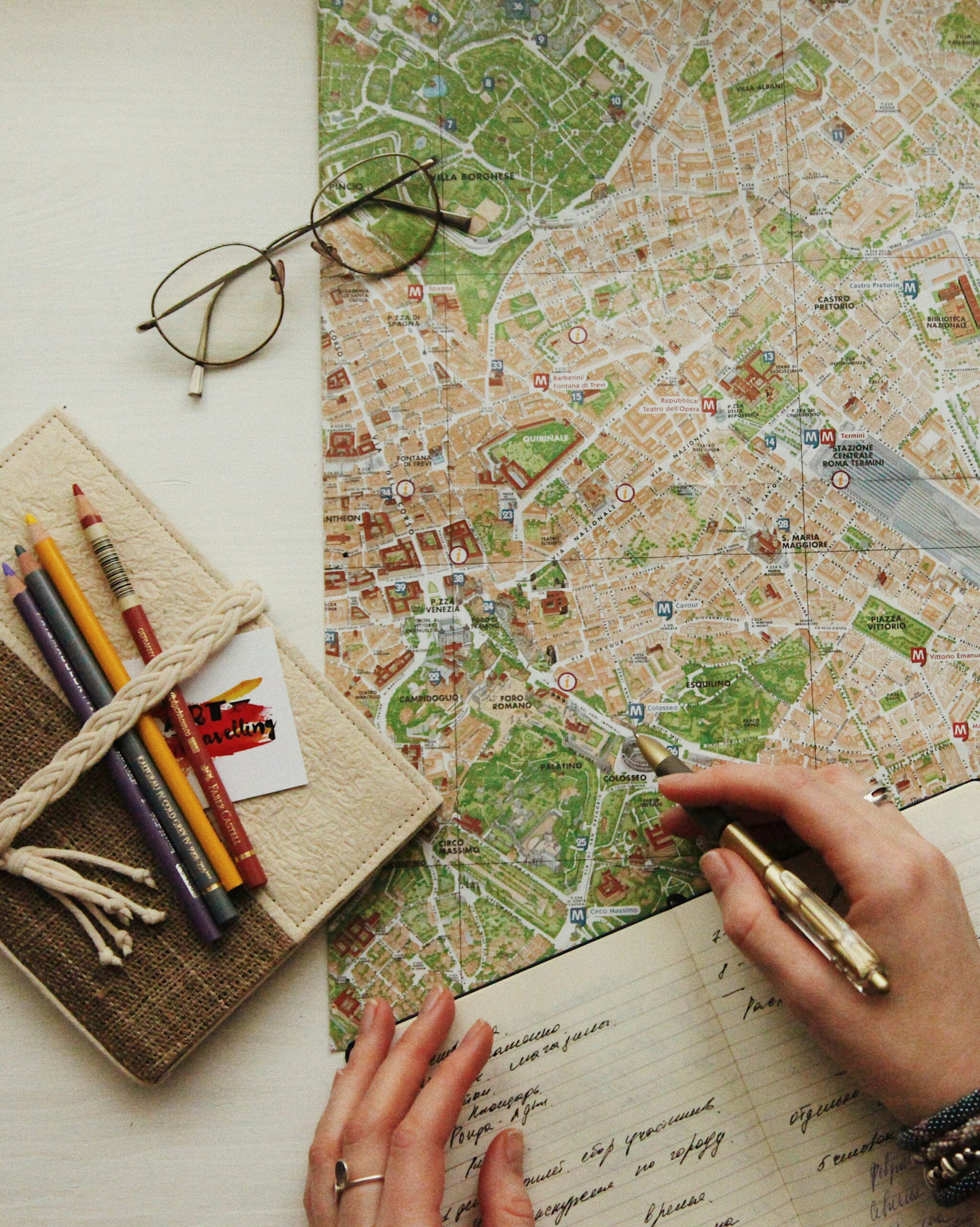 A hand marking up a city map with a notebook and glasses nearby